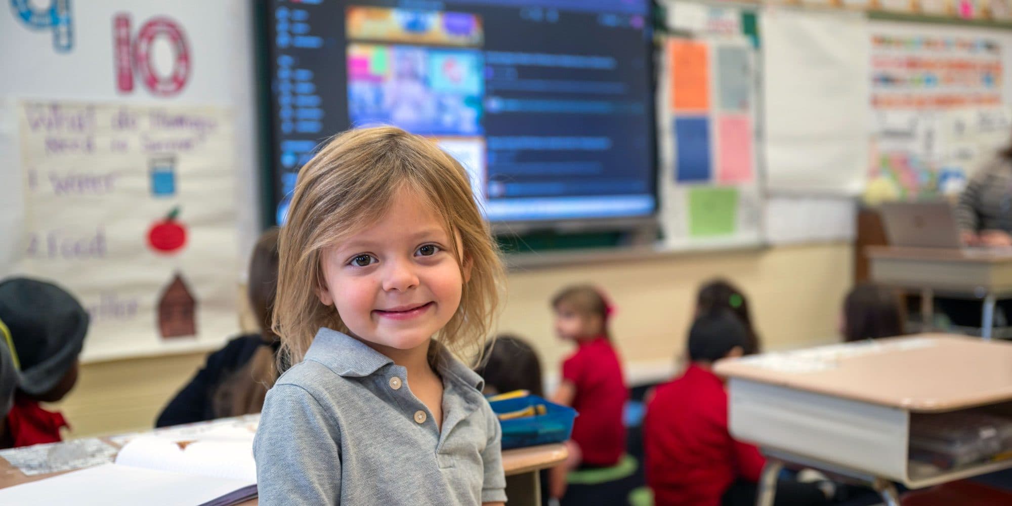 Smiling student at a desk in front of a classroom screen.