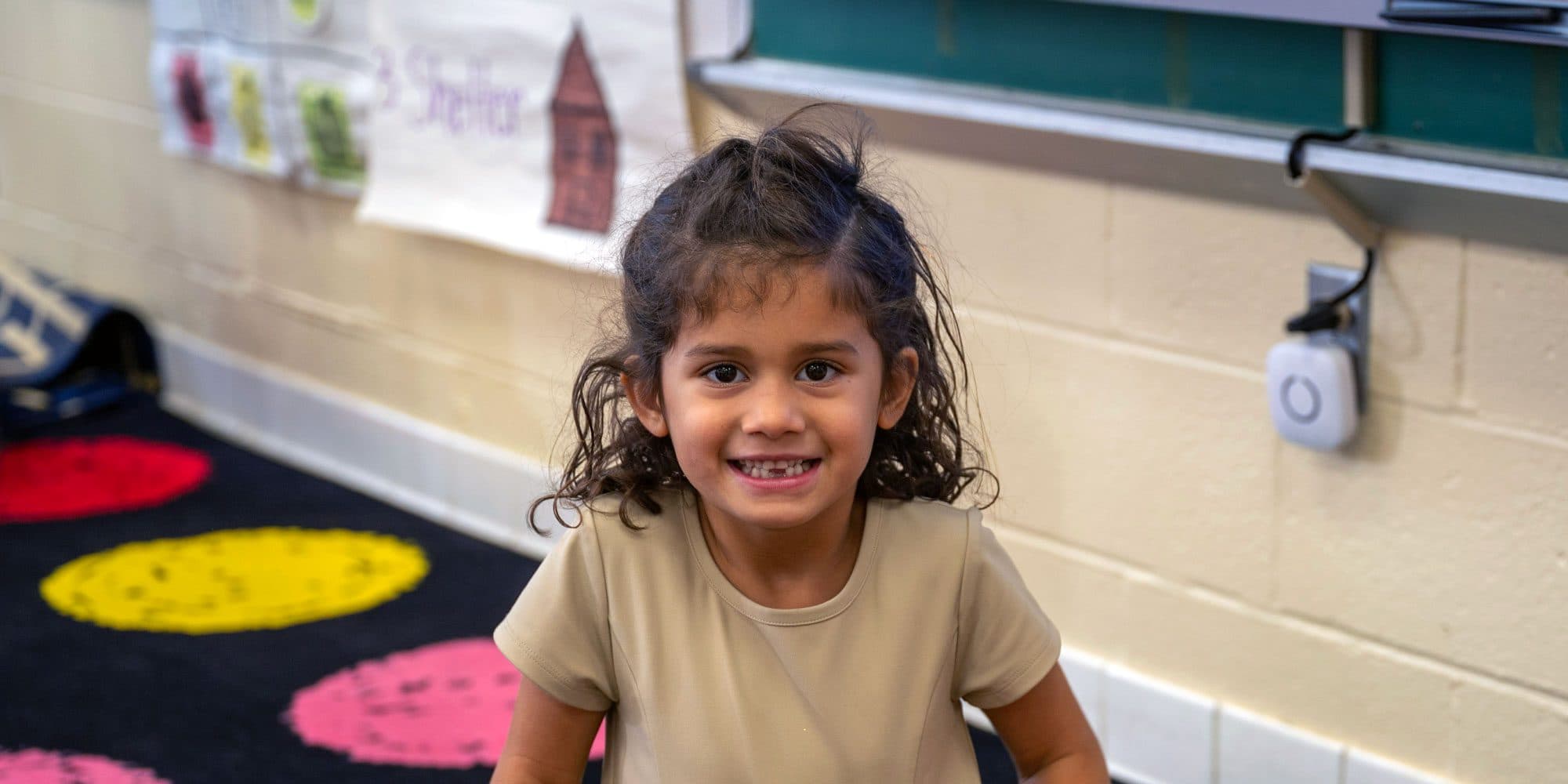 Smiling student sitting on a colorful classroom rug.