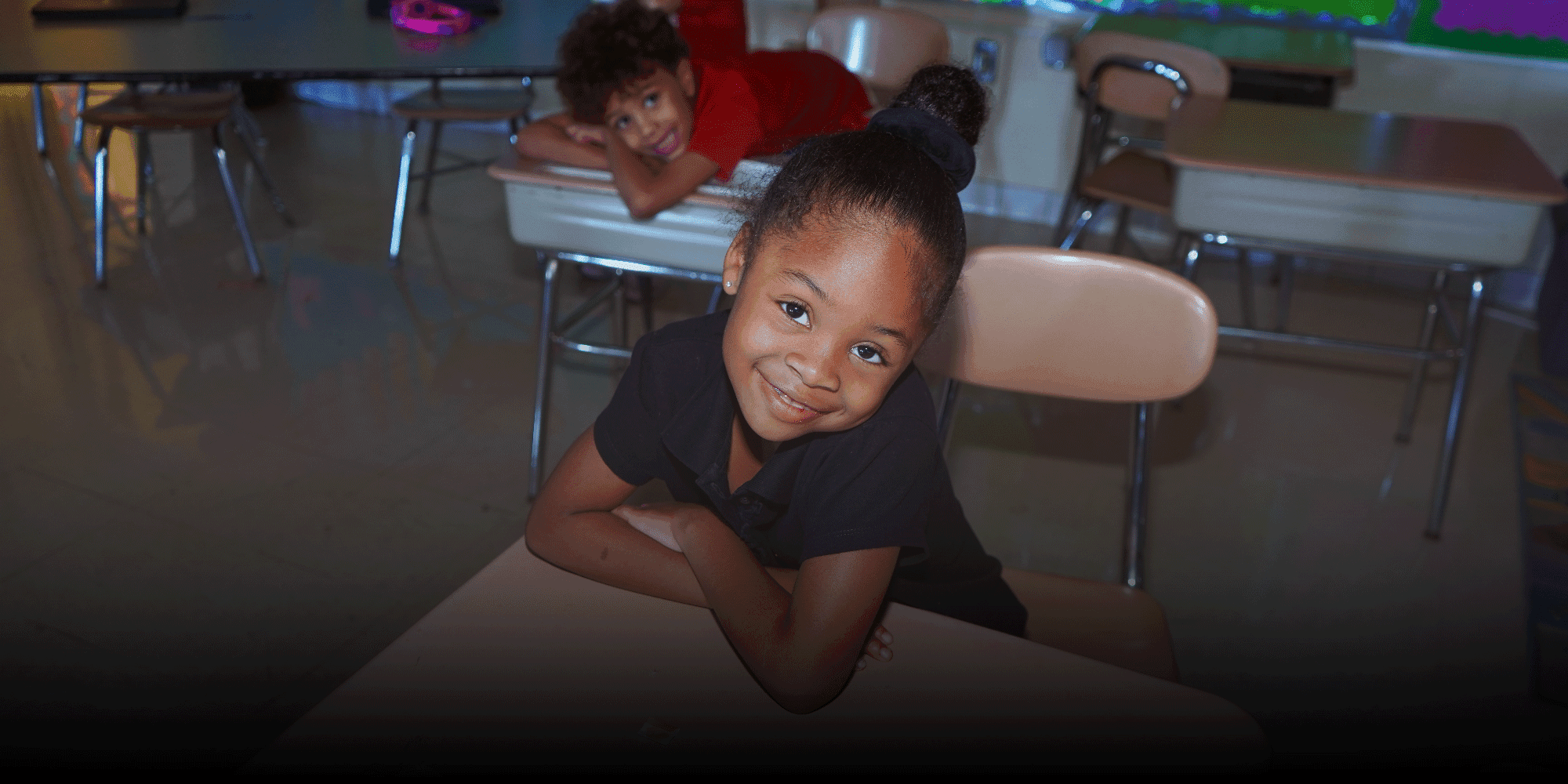 Smiling student resting on a classroom desk.