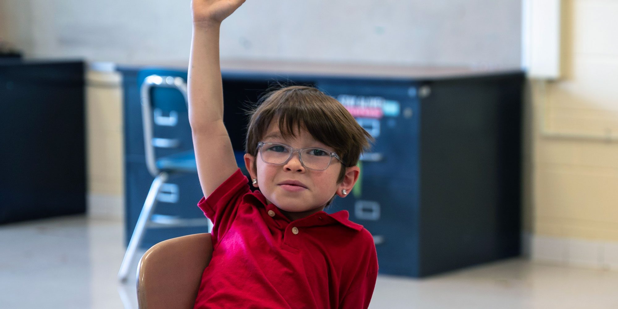Student in glasses raising a hand in class.