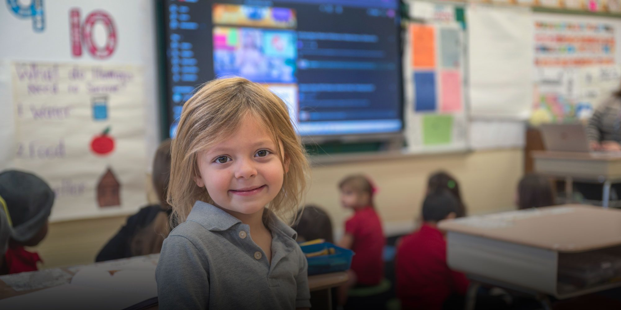 Elementary student smiling and sitting in front of school board
